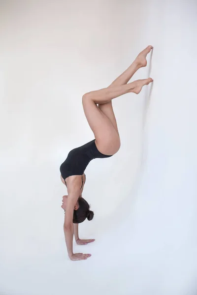 Young woman gymnast stands in a gymnastic position on a white background.
