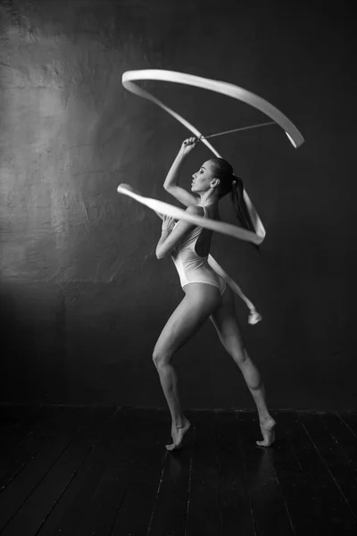 Mulher bonita ginasta com uma fita branca em um fundo preto . — Fotografia de Stock