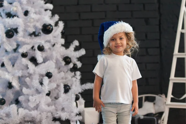 Jolie petite fille dans un T-shirt blanc est debout près du sapin de Noël. Maquette . — Photo