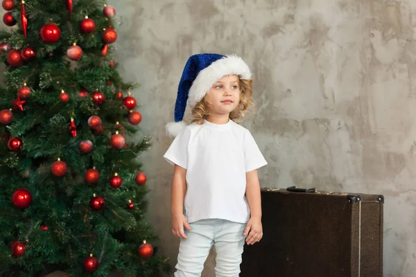 Jolie petite fille dans un T-shirt blanc est debout près du sapin de Noël. Maquette . — Photo