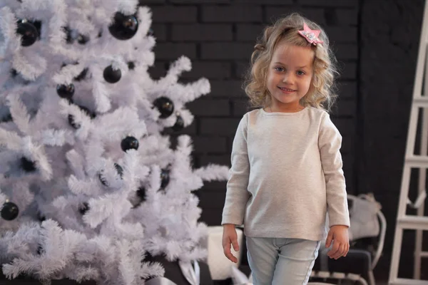 Uma menina bonita em uma camisola cinza em branco perto da árvore de Natal. Faz asneira. . — Fotografia de Stock