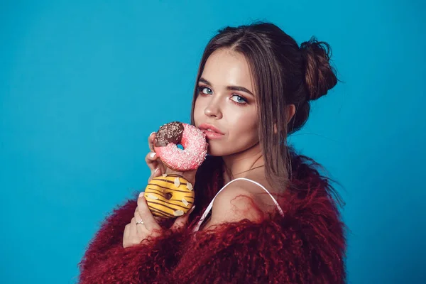 Привлекательная молодая женщина в яркой шубе позирует с пончиками в руках . — стоковое фото