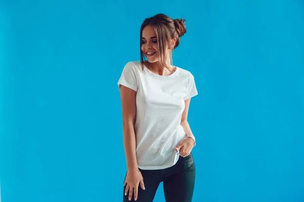 Una atractiva mujer con una camiseta blanca está de pie sobre un fondo azul. Mock-up . —  Fotos de Stock