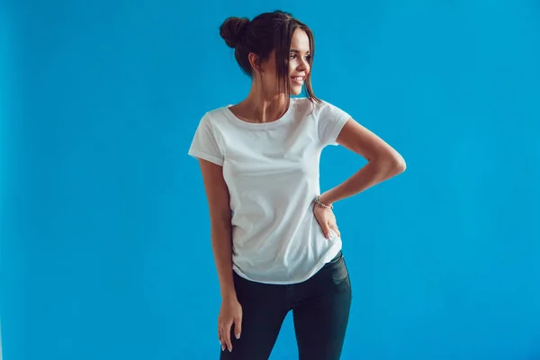 Attractive woman in a white t-shirt stands on a blue background. Mock-up. — Stock Photo, Image