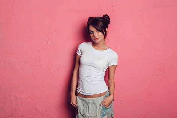 Attractive woman in a white t-shirt stands on a pink background. Mock-up. — Stock Photo, Image