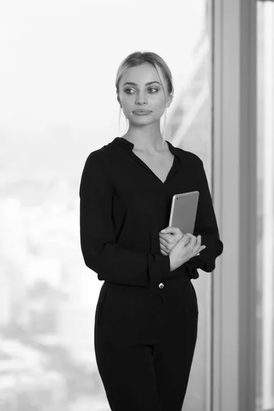 Schöne Geschäftsfrau mit Tablet in der Hand steht neben Fenster im Büro. — Stockfoto