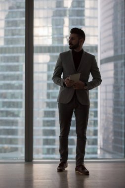Onun elinde bir tablet ile işadamı şehir manzaralı bir pencere yakınında duruyor.