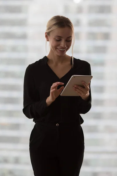 Beautiful business woman with tablet in hands stands near window in office.