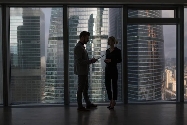 Business people talking negotiating standing near large panoramic window with big city buildings.