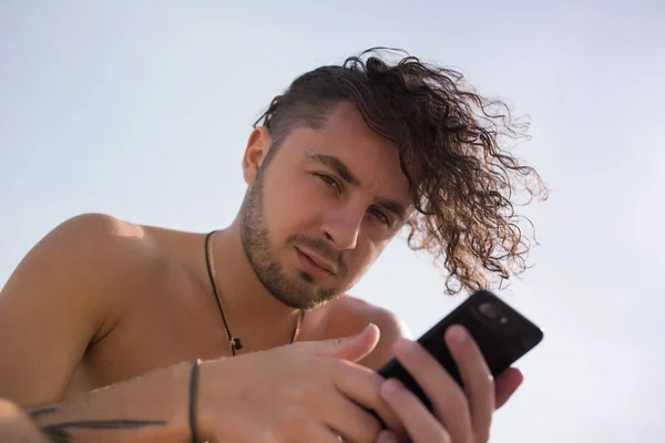 En man med lockigt hår använder en smartphone. — Stockfoto