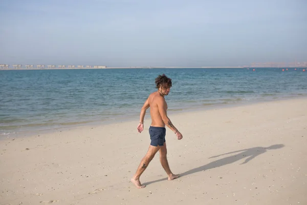 Jeune homme marchant le long de la plage . — Photo