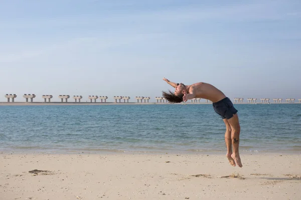 Jeune homme faisant un saut périlleux sur la plage . — Photo