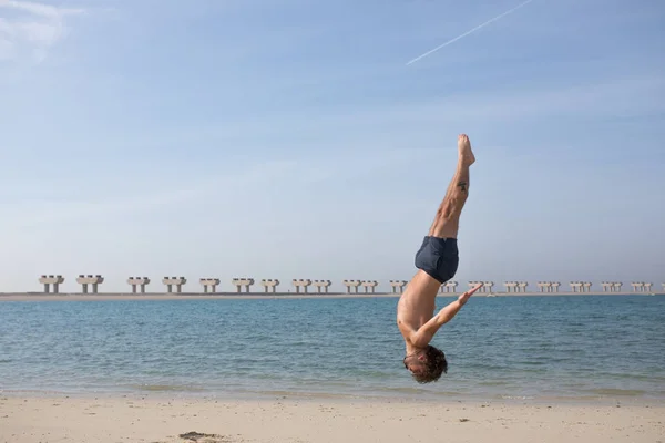 Młody człowiek robi Salto na plaży. — Zdjęcie stockowe