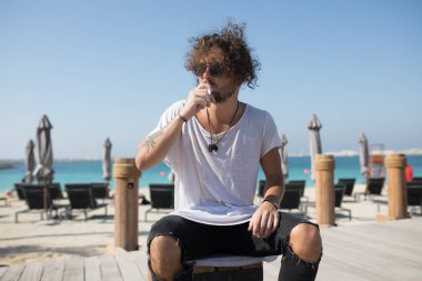 Plaja yakın oturan ve sigara şık adam.