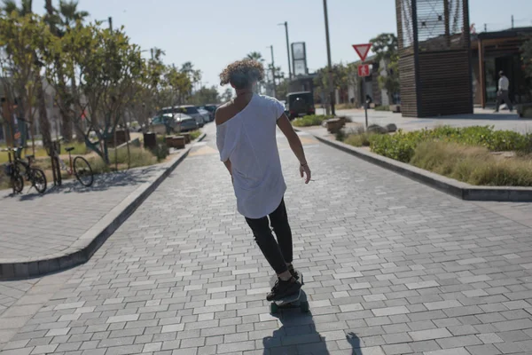 Een jonge man in een wit t-shirt rijden een skateboard op de straat. — Stockfoto