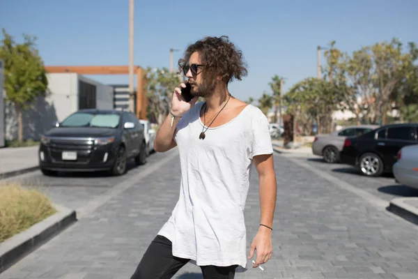 Ο άνθρωπος σε ένα άσπρο T-shirt καπνίζει και μιλάει στο τηλέφωνο. — Φωτογραφία Αρχείου
