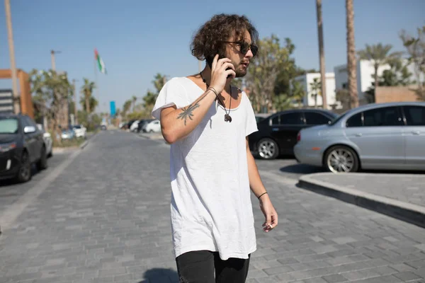 Man in een wit T-shirt rookt en spreekt over de telefoon. — Stockfoto