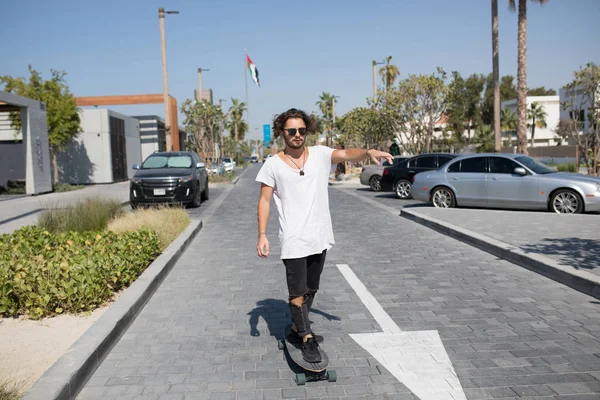 Een jonge man in een wit t-shirt rijden een skateboard op de straat. — Stockfoto