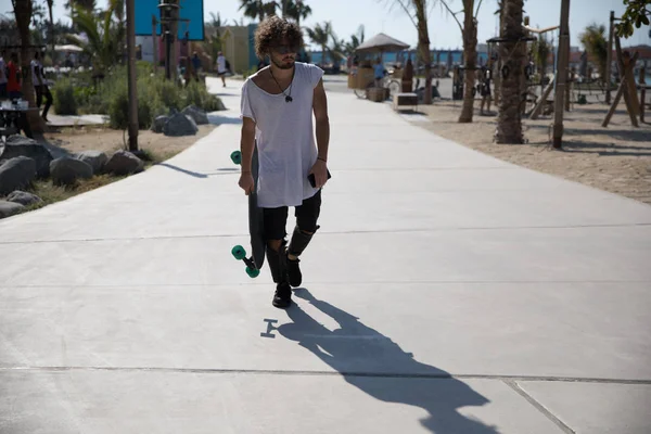 Stijlvolle man lopen in de straat met een skateboard. — Stockfoto