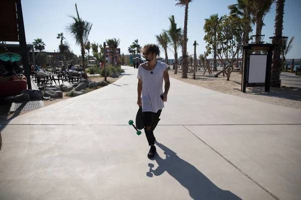 Stijlvolle man lopen in de straat met een skateboard. — Stockfoto
