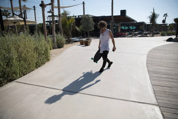 Stijlvolle man lopen in de straat met een skateboard. — Stockfoto