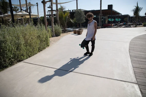 Stijlvolle man lopen in de straat met een skateboard. — Stockfoto