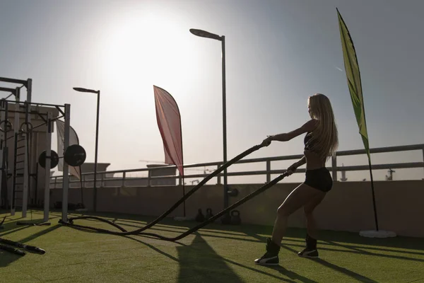 Mujer deportiva haciendo ejercicios de cuerdas de batalla en un gimnasio de entrenamiento cruzado . — Foto de Stock