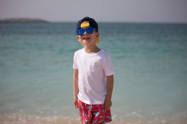 Küçük çocuk güneş gözlüğü deniz arka plan üzerinde duruyor.