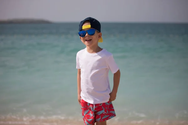 Mały chłopiec w okulary stoi na tle morza. — Zdjęcie stockowe