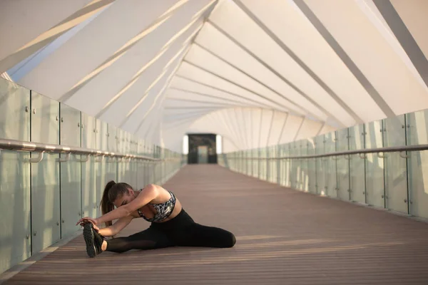 Αθλητικά γυναίκα κάνει τεντώνοντας ασκήσεις σε μια γέφυρα. — Φωτογραφία Αρχείου