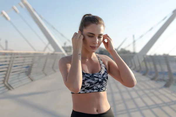 Young sporty woman with earphones listening to music outdoors.