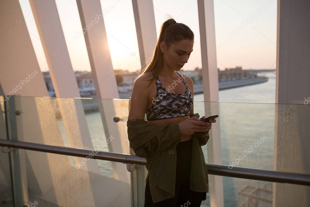 Attractive girl uses a smartphone on sunset background.