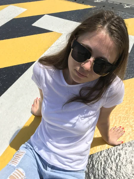 Menina atraente em uma camiseta branca está sentado na estrada. Mock-up . — Fotografia de Stock