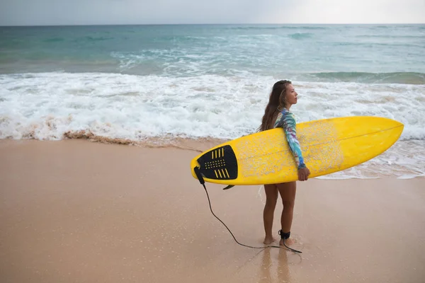 Жінка-серфер дивиться на океан з дошкою для серфінгу в руках . — стокове фото