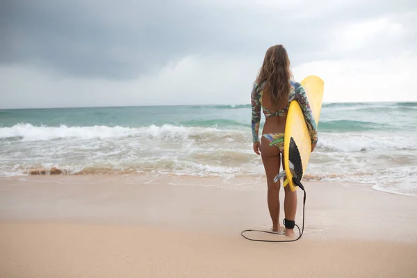 Kvinna surfare tittar på havet med en surfbräda i hans händer. — Stockfoto