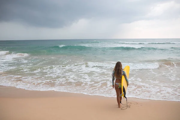 Kvinna surfare tittar på havet med en surfbräda i hans händer. — Stockfoto