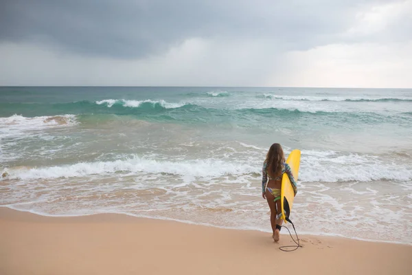 Kvinna surfare tittar på havet med en surfbräda i hans händer. — Stockfoto