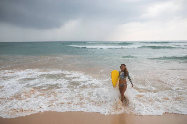 Vacker kvinna surfer utgångar från havet med en surfbräda i händerna. — Stockfoto