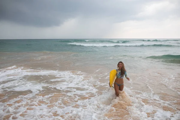 Vacker kvinna surfer utgångar från havet med en surfbräda i händerna. — Stockfoto