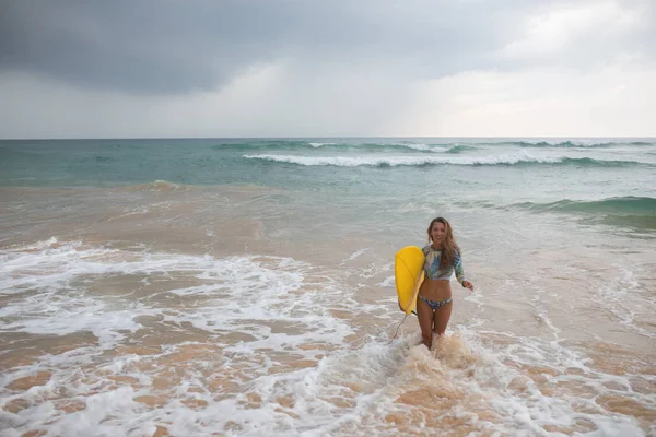 Vacker kvinna surfer utgångar från havet med en surfbräda i händerna. — Stockfoto
