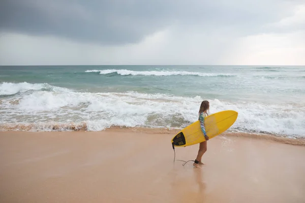 Vacker kvinna surfare står på ocean bakgrunden med surfbräda i händer. — Stockfoto