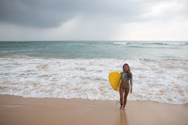 Vacker kvinna surfare står på ocean bakgrunden med surfbräda i händer. — Stockfoto