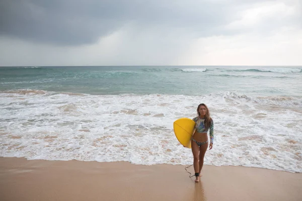 Vacker kvinna surfare står på ocean bakgrunden med surfbräda i händer. — Stockfoto