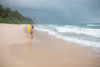 Kadın sörfçü eller bir yönetim kurulu ile okyanus boyunca yürüyüş.
