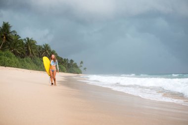 Kadın sörfçü eller bir yönetim kurulu ile okyanus boyunca yürüyüş.