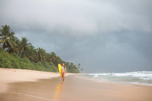 Kvinnliga surfare promenader längs havet med en styrelse i händer. — Stockfoto