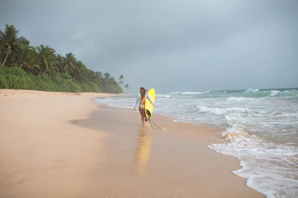 Kvinnliga surfare promenader längs havet med en styrelse i händer. — Stockfoto