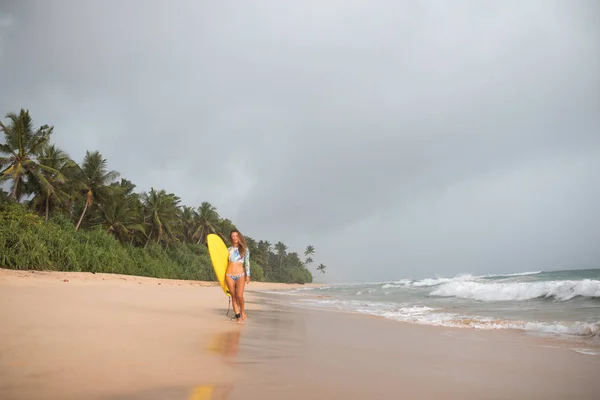 Kvinnliga surfare promenader längs havet med en styrelse i händer. — Stockfoto