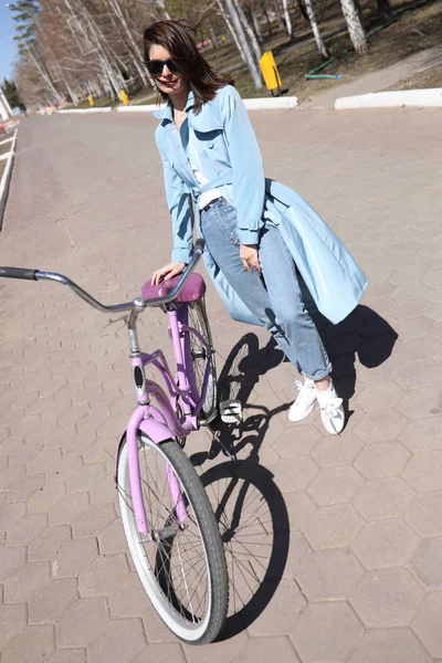Стильная молодая женщина, идущая по улице с велосипедом . — стоковое фото