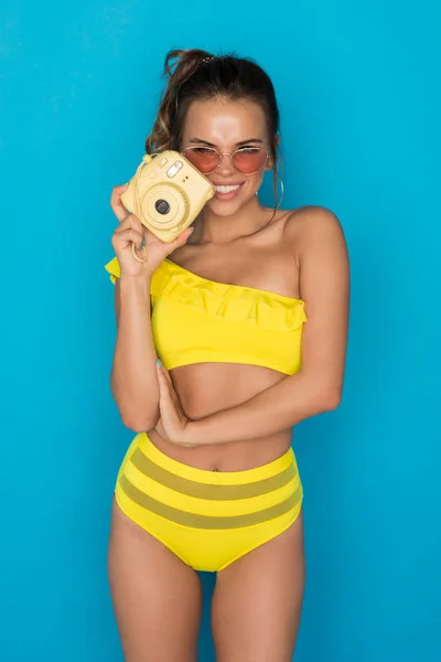 Sexy young woman in a bright yellow swimsuit with a polaroid in her hands. — Stock Photo, Image